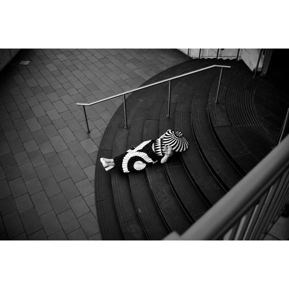 Overhead black-and-white fashion photograph on a curved staircase