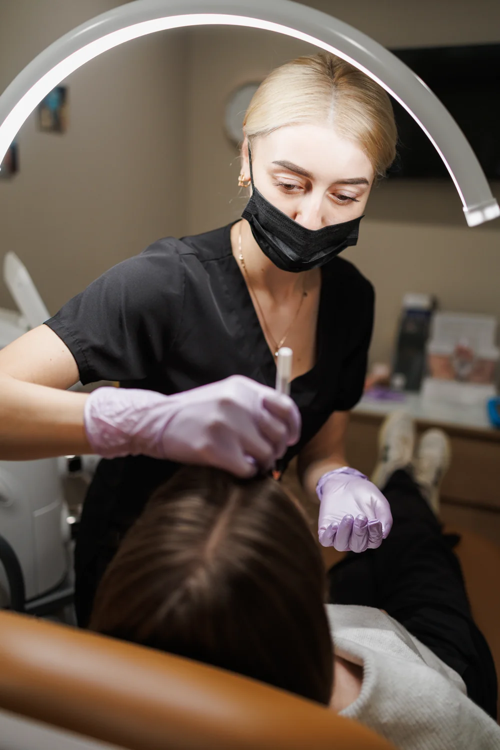 A woman wearing gloves and a face mask working beside a reclining client